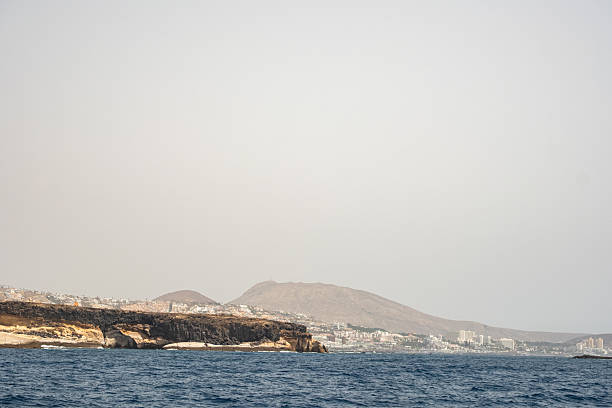 Coastal landscape with distant mountains and calm ocean horizon under clear sky.