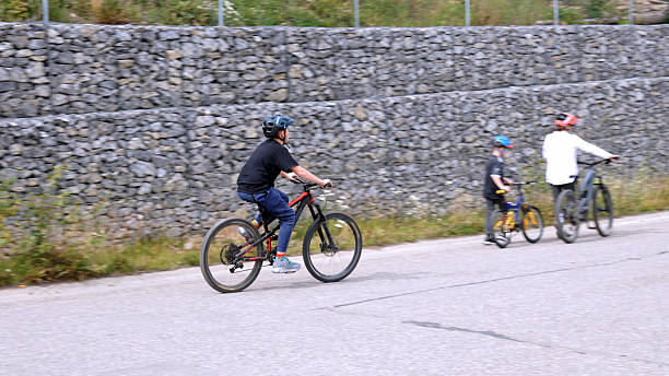 Toddler boy riding red balance bike on asphalt track, wearing helmet and green shirt, focused face, developing balance and motor skills, enjoying active outdoor playtime and cycling training.