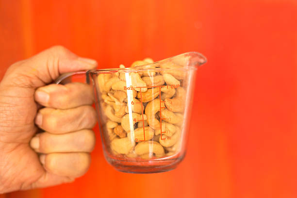 Man's Hand Holding Measuring Cup Cashews, Red Background