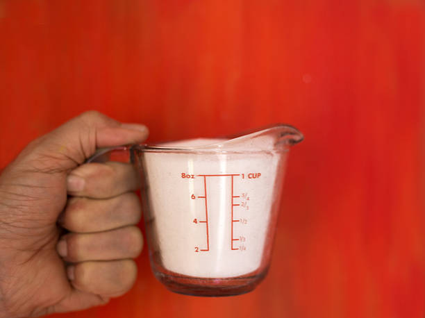 Man's Hand Holding Measuring Cup White Sugar, Red Background