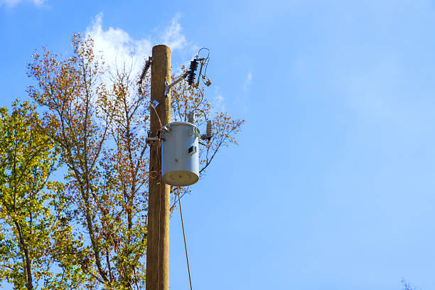 Utility pole with transformer against trees in suburban area during works day