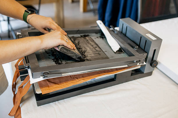 istock Manual Silk Screen Printing on Fabric – Close-up of Hands Working with Screen Printing Machine in Workshop 2231595900