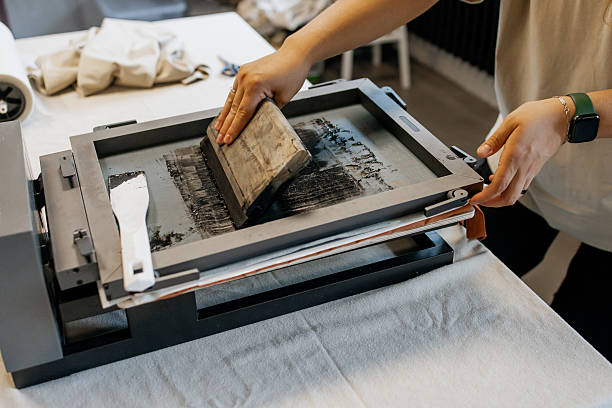 istock Manual Silk Screen Printing on Fabric – Close-up of Hands Working with Screen Printing Machine in Workshop 2231595923