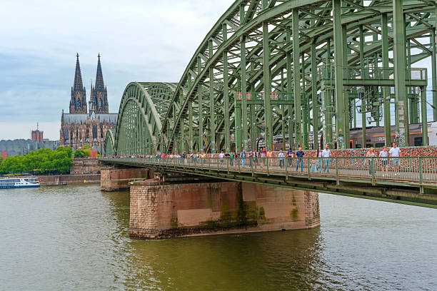 Cologne, Germany - June 15, 2025: Hohenzollern Bridge arches over the Rhine River with the Cologne Cathedral in the background, showcasing a blend of architecture and scenic beauty.