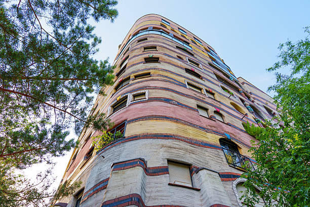 Darmstadt, Germany - June 18, 2025: Curved facade of Waldspirale residential complex, featuring colorful stripes and unique architectural design, surrounded by greenery in Darmstadt, Germany.