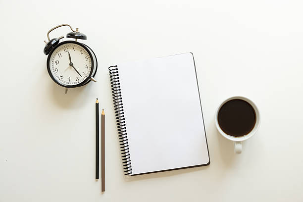 Black coffee, notebook, pencils and alarm clock on white table