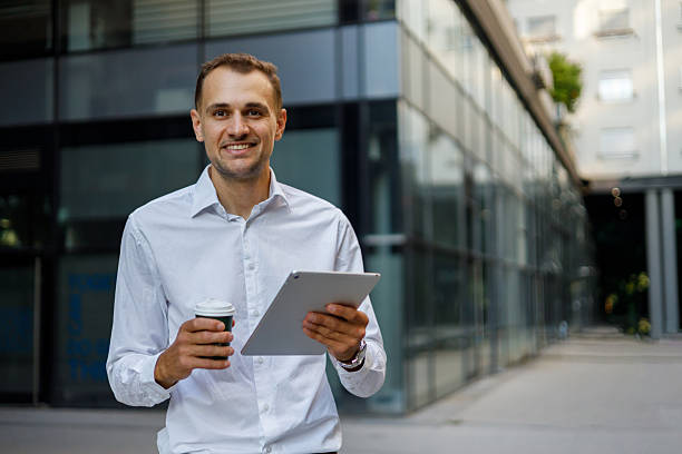 istock Professional businessman smiling, working on digital tablet while drinking coffee outdoors 2231610831