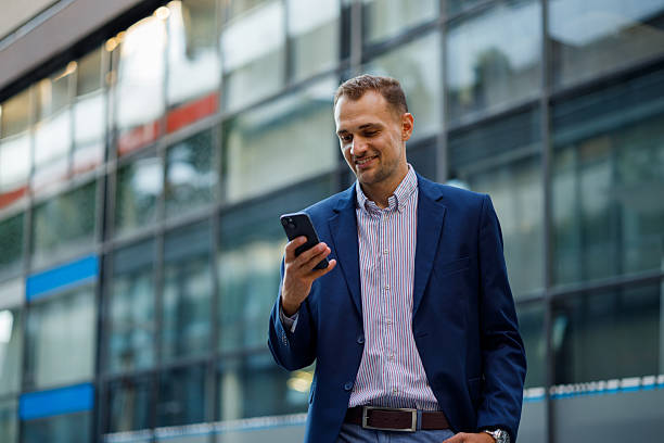 istock Professional businessman using smartphone, standing near sleek office building, radiating corporate success and confidence 2231611416