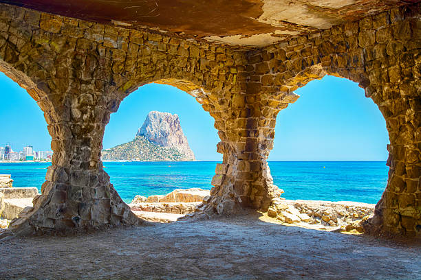 Stone archways framing a breathtaking view of the Mediterranean Sea and the iconic Peñón de Ifach rock in Calpe, Spain