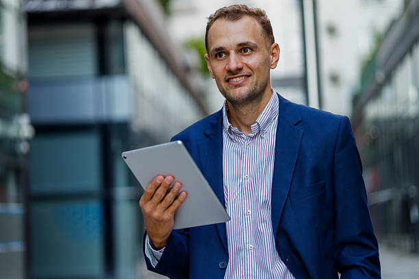 istock Young businessman smiling while walking through a bustling city street, engaging with a digital tablet and enjoying modern technology 2231613272