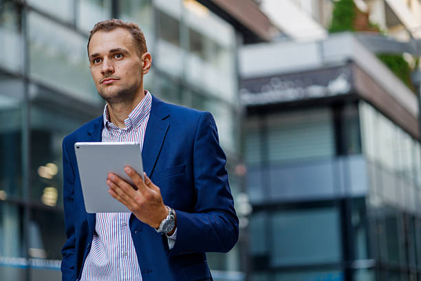 istock Businessman walking outside an office building while holding a digital tablet, engaging with technology in a modern urban environment 2231613722