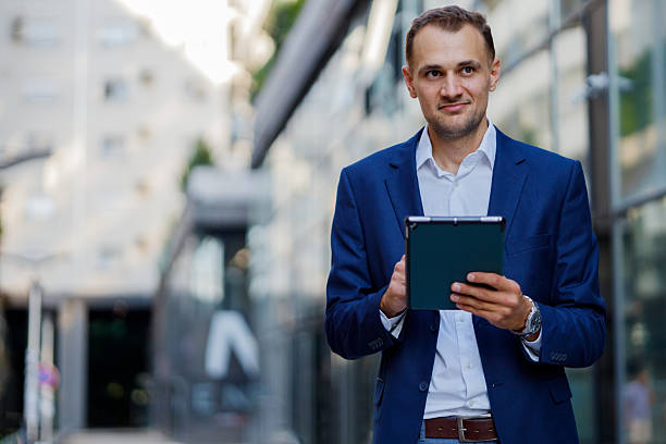 istock Professional businessman walking urban street, utilizing digital tablet while wearing tailored suit amid city movement 2231615895