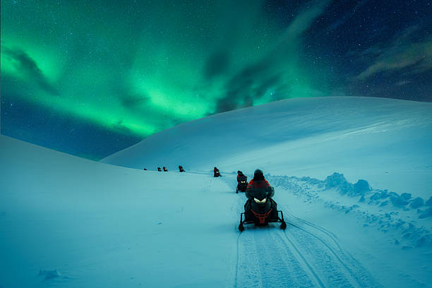 Snowmobile adventure across snowy mountain track with aurora borealis in winter stock photo