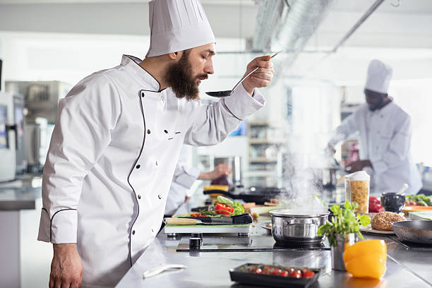 istock Professional chef in uniform tasting a savory sauce from a pan on the stove 2231626463
