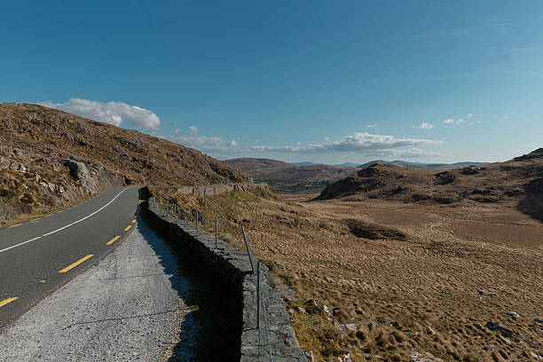 Winding Irish mountain road with stone wall through rugged highland terrain
