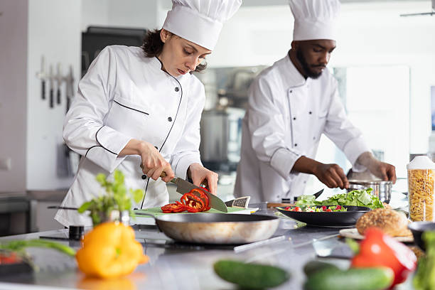 istock Woman chef in uniform slicing a bell pepper in professional kitchen 2231630257