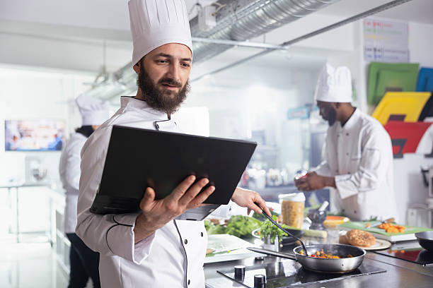 istock Head chef in a professional kitchen uses a laptop to refine recipes 2231631591