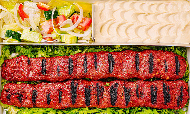 Grilled kebabs served with fresh salad and hummus in takeout container