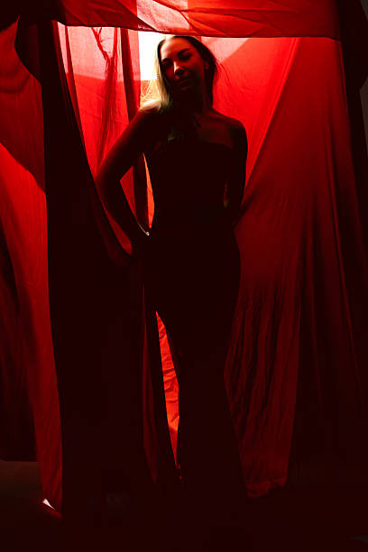 istock Silhouette of a woman standing gracefully behind red fabric in a dimly lit studio environment during an artistic photoshoot 2231637101