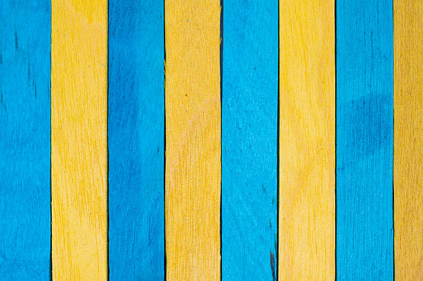 Vertical alignment of alternating blue and yellow wooden sticks, creating a structured, rhythmic pattern. A clean and bold visual emphasizing contrast and repetition.