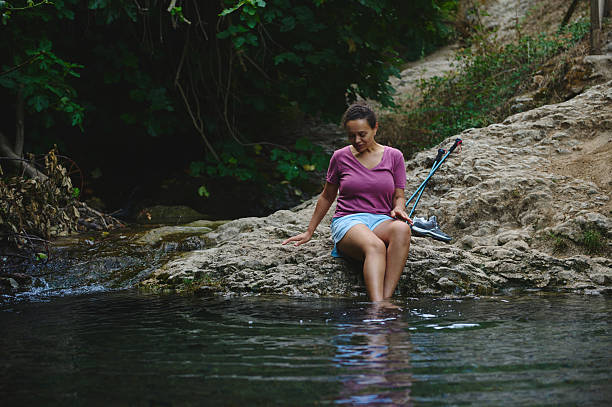 Woman Relaxing by a Serene Stream in a Forested Environment