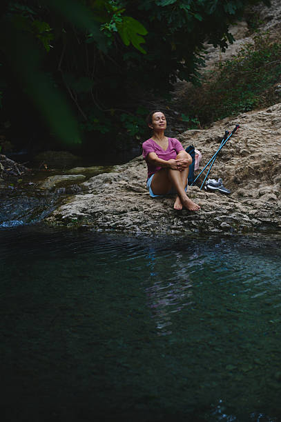 istock Woman Relaxing by a Tranquil Forest Stream with Trekking Gear 2231643233