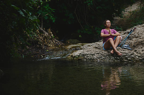 istock Woman Practicing Meditation by a Serene Stream in Lush Natural Setting 2231643321