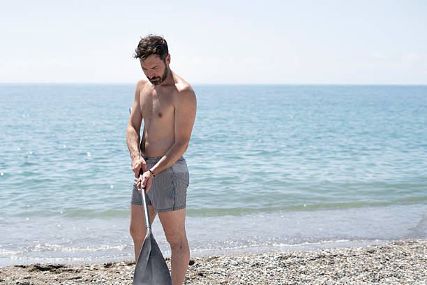 Man holding paddle, preparing paddle board on beach for stand up paddling in ocean