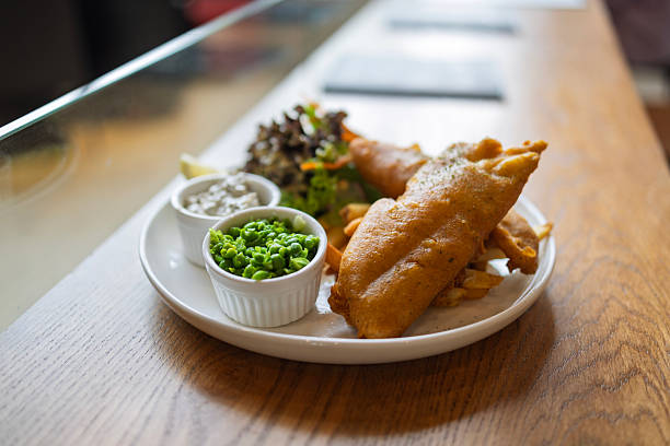 Close-up of a traditional British fish and chips meal served with mushy peas, tartar sauce, and fresh salad on a white plate in a restaurant.
