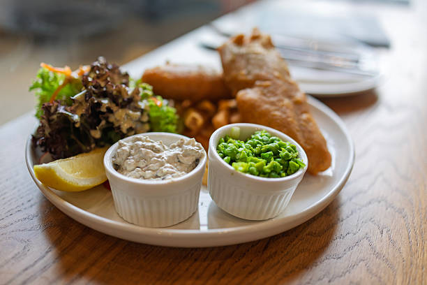 Carton of Traditional Fish and Chips with mushy peas being held above Towan Beach, Newquay, Cornwall on a wet June day.