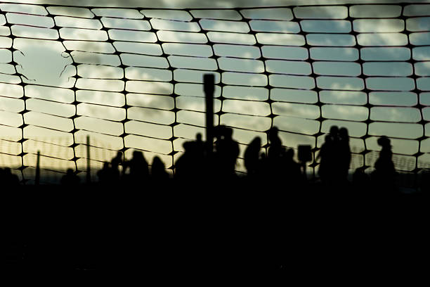 Unidentified people blurred in silhouette behind a plastic fence during a dramatic sunset. Winter season. Tourists traveling.