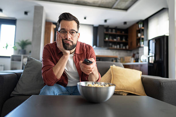istock Bored young man watching television and holding remote control 2231652331