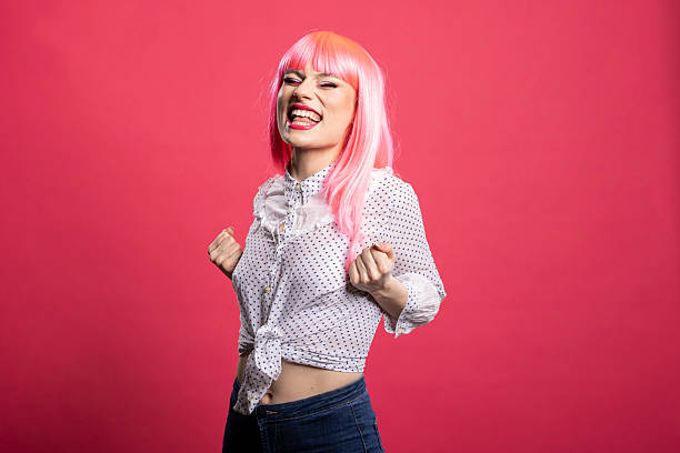 Tokio street style fashion. Japanese woman in a drag outfit and pink hair do and rainbow make-up against a gray backdrop. Studio shot.