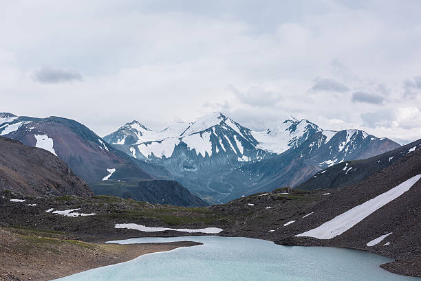 istock Dramatic view to most beautiful blue alpine lake against snow-covered range with few pointy peaks. Atmospheric landscape with azure mountain lake against three snowy peaked tops under gray cloudy sky. 2231656546