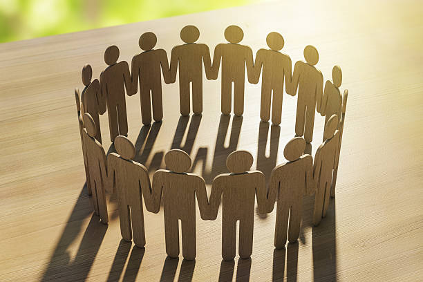 istock Wooden human figures holding hands in a circle symbolizing unity and support on a wooden surface under warm sunlight with soft background. 3D Rendering 2231657975