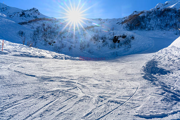 The bright sun shines down on a snowy ski slope, with ski tracks visible on the fresh snow. The panoramic view captures the majestic mountains in the distance, perfect for outdoor enthusiasts.