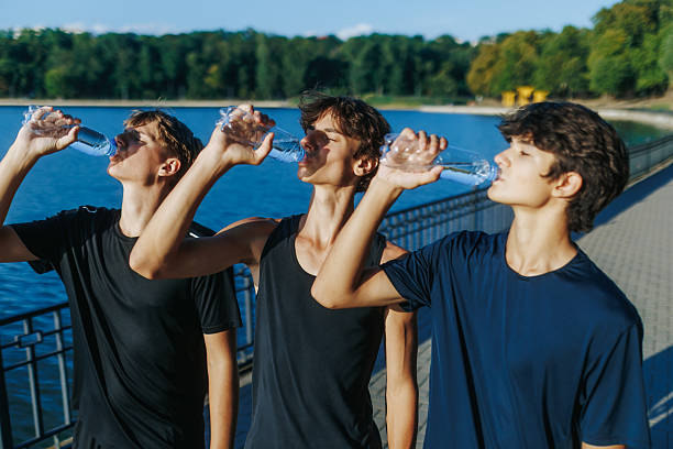 Three teenagers drink water together after outdoor running at sunset, enjoying hydration and energy. A healthy lifestyle moment filled with joy and friendship.