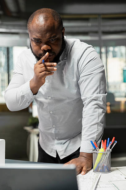 istock Black male engineer looking at blueprints plans on laptop for construction site 2231668454