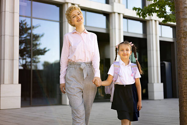 A mother and daughter walk hand in hand in front of a school building, a moment of connection and love.