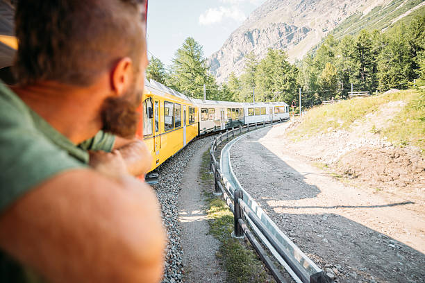 istock Man Watching Yellow Train Travel Through Mountains 2231669881