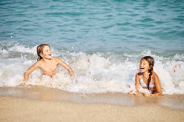 Young caucasian boy and girl jumping into waves. They are swimming and diving in clear turquoise colored sea.