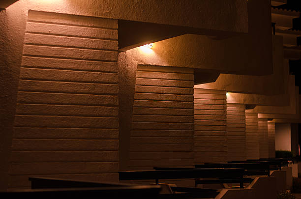 Modern hotel exterior at night with warm lighting casting shadows on geometric walls. Dark ambiance with muted tones creates serene and inviting atmosphere
