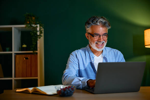 istock Smiling mature man working from home at night using laptop 2231676029