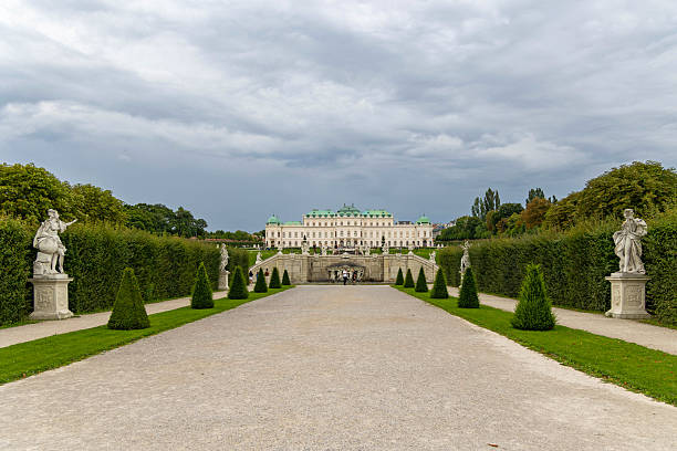Vienna, Austria - August, 01, 2025: Wide-angle view of Belvedere Palace in Vienna, Austria, featuring symmetrical hedges, statues, fountains, and a dramatic cloudy sky