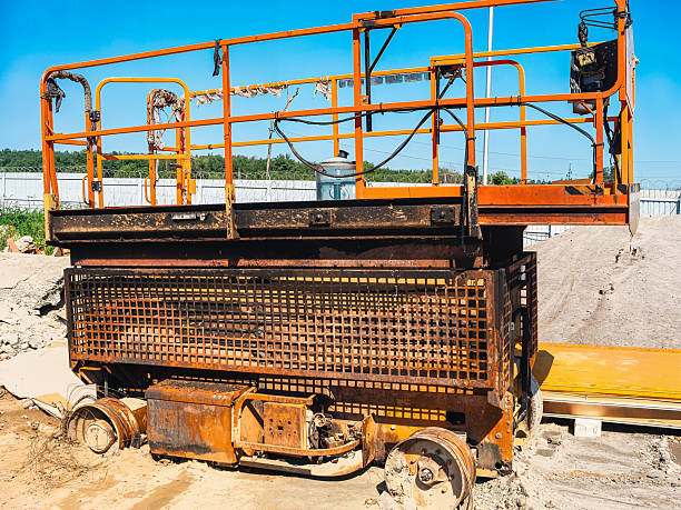 istock An old, orange construction lift is shown outdoors against a bright blue sky. 2231681526