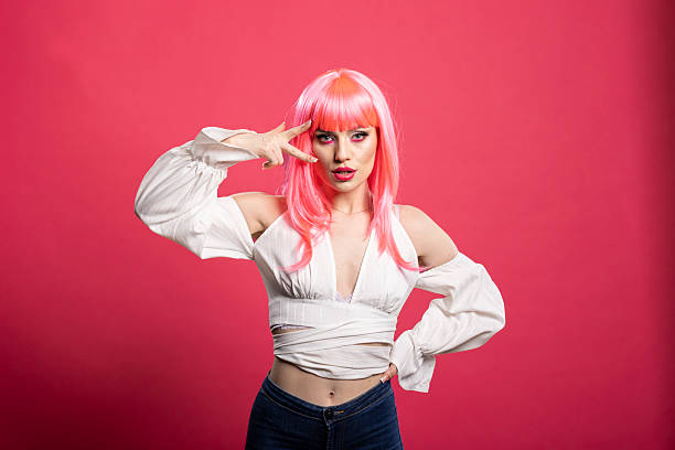 Fashionable woman with playful pose flashes peace sign, puckering lips against pink background. Young model with carefree charm smiles with confidence and expressive face during fun studio shoot.