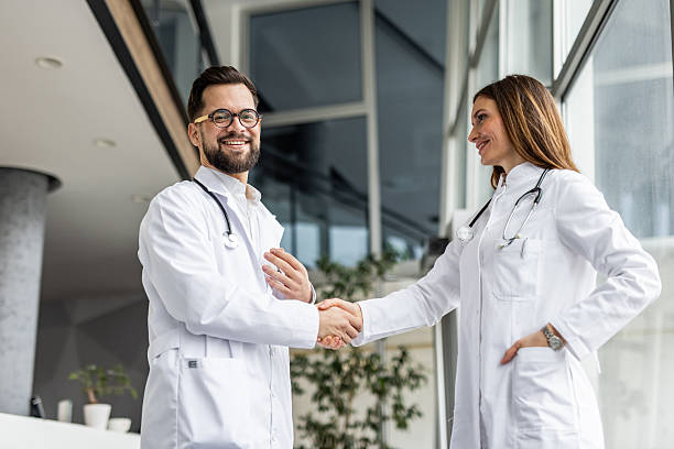 istock Two smiling doctors shaking hands in hospital lobby 2231695694