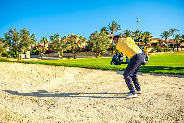 A golfer flattens the sand in the bunker with a rake to hit a shot with his golf club