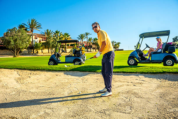 istock Golfer playing from sand trap on sunny golf course with golf carts 2231697086