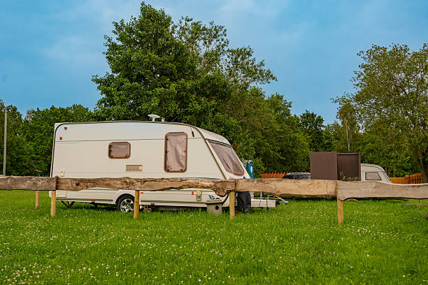 White caravan parked peacefully in a lush green field, surrounded by trees under a cloudy sky. Ideal for outdoor travel and leisure